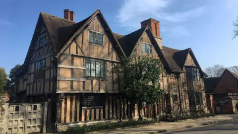A timber‑framed house with steep roofs on a street under a clear blue sky. 