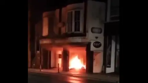 A fire in the ground floor of a two-storey building at night.