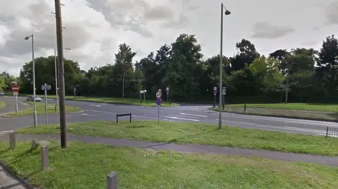 A road junction which features lampposts and grass verges and one road has a no entry sign.