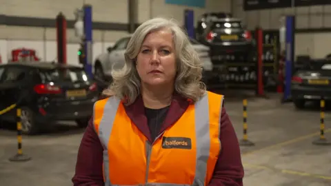 The Transport Secretary Heidi Alexander wears a Halfords orange high vis jacket and stares directly at the camera. 