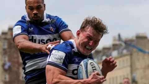 PA Media A close up of Ted Hill scoring a try at the Bath recreation ground, collecting the ball with a very tense look on his face and a team player right behind him.