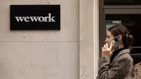 A woman talking on a cell phone walks past a WeWork co-working office space in New York, US, on Tuesday, Nov. 7, 2023. 