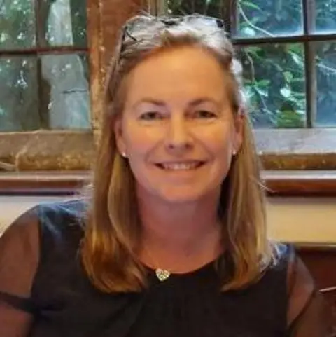 Andrea Lord A woman with blonde hair and a black top sits in front of a window.