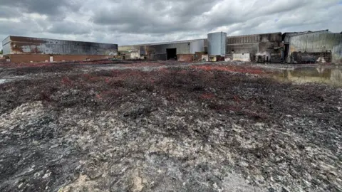 Northamptonshire Fire and Rescue Service A burnt out building, showing burnt ground and burnt metal buildings.