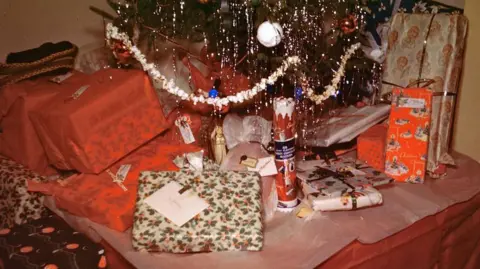 AFP via Getty Images A scene from the 1940s, a coloured picture which shows presents in red and holly covered wrapping paper under a Christmas tree with tinsel. 