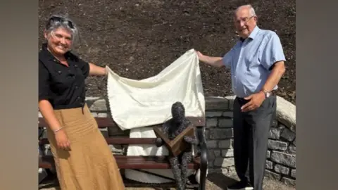 Lyme Regis Town Council Artist Vik Westaway and town mayor Philip Evans unveiling the sculpture on a park bench