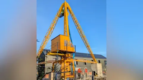 Simon Pattern The Scotch Derrick crane in position at the North End Shipyard. The crane is bright yellow and is in the shape of something resembling a Christmas tree. The cab is in the centre - and the arms of the crane come out like Christmas tree branches and converge in a point at the top. 