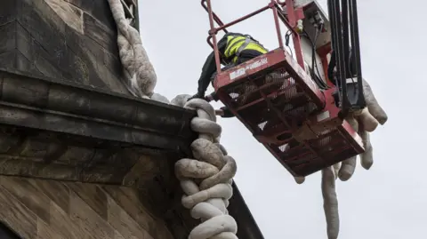 Yorkshire Sculpture Park/Nicola Turner A person on a red cherry picker arranges wool sculptures at the top of a building