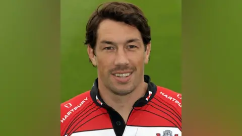 Getty Images Foto kepala dan bahu Tom Voyce dalam perlengkapan rugby Gloucester. Ini adalah kemeja melingkar merah dan putih dengan logo perusahaan Jewishon di bagian dada.