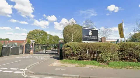 Google Outside view of Hampton Boys school showing the school gates and sign. It's a sunny day. 