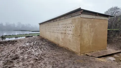 A long sandy coloured flat roofed building with small circular holes along one side provides burrows for the sand martins to nest in 