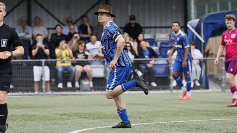 Margate FC Pete Doherty running on a football pitch. He is wearing a blue kit and a brown hat.