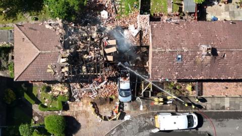 A drone picture of the damaged house, missing its roof, surrounded by debris