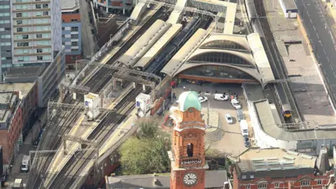 NetworkRail Railway tracks snake past Manchester Oxford Road train station, which is pictured from the sky. Cars can be seen park in the turning circle outside the station, with the view obstructed by the Kimpton Clocktower.