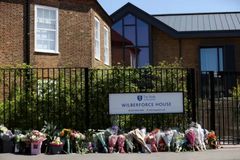 PA Media Floral tributes are laid outside a school gate under a sign for Wilberforce House