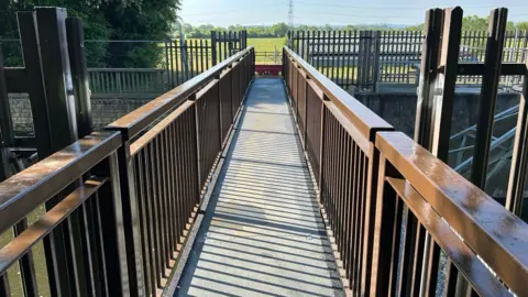 Narrow metal footbridge, viewed from one end, looking along the walkway 