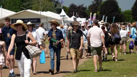 crowds milling at the Royal Norfolk Show wearing shorts and shirts and sunglasses with marquees in the background