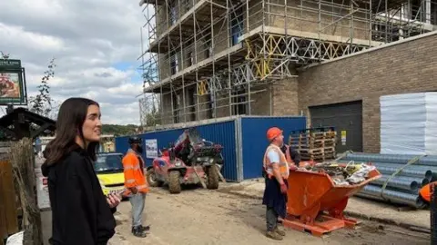 Nina Hristova Property being built with scaffolding around it with two builders in orange clothing looking up at the building.