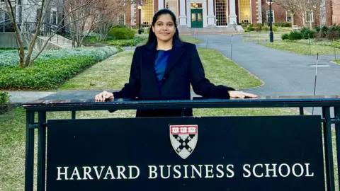 Shreya Mishra Reddy stands behind a sign with the words Harvard Business School and a crest of the institution at its campus in Boston in the United States.