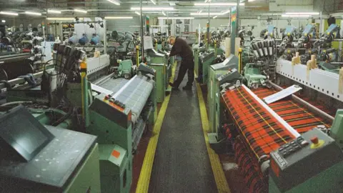 Alchemy Festival A man bends over a machine at the centre of a Borders textile factory