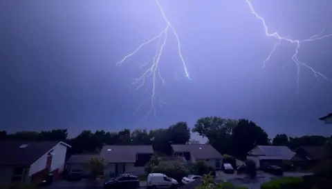 Blue sky with fork lightning above homes and trees