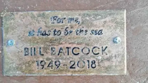 Familyphotograph A weathered metal plaque nailed into a piece of wood bearing the words: "For me, it has to be the sea," above the inscription: "Bill Batcock - 1949 - 2018."