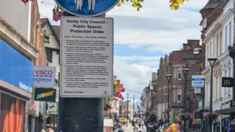 A PSPO sign attached to a lamppost in a busy St Peters Street in Derby