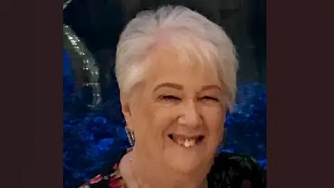 Connie Fish smiles at an event. She has short white hair and wears a dark floral printed top.