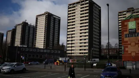 Reuters A woman walks in front of the Seven Sisters residential tower blocks in a car park on a cloudy day in Rochdale