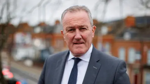 PA Media Murphy is looking directly at the camera. He is wearing a grey suit and tie and a white shirt. He has short grey hair.