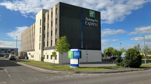 A Holiday Inn Express hotel by a road. it's a box-shaped building with four stories.