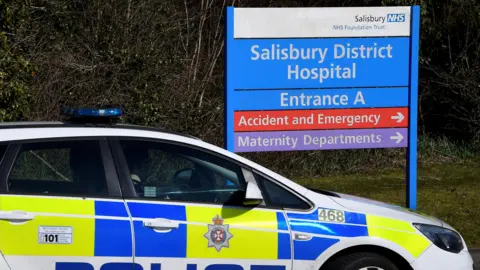 Reuters A police car, parked next to a large blue and white sign which says "Salisbury District Hospital". 