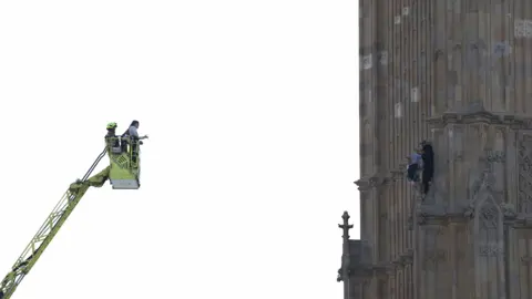 PA Media Emergency workers on an extendable ladder speak to the man on Elizabeth Tower