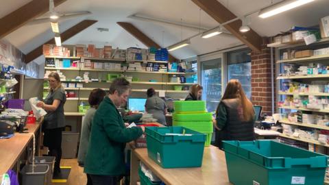 Staff work in a busy room surrounded by shelves of medication