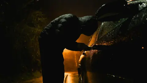 Man with hood trying to break into car.