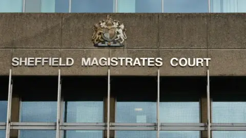 The exterior of Sheffield Magistrates' Court, with the name of the court in white writing. Above it is a crest, with a row of windows beneath the sign.