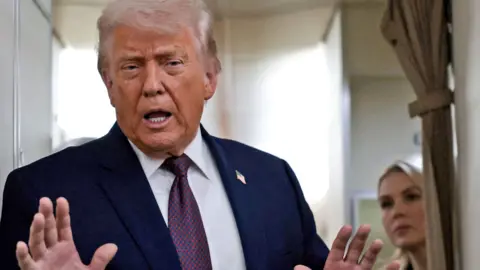 Reuters President Trump talks to reporters on Air Force One on Thursday. He is holding both hands up and Press Secretary Karoline Leavitt is watching on from behind.