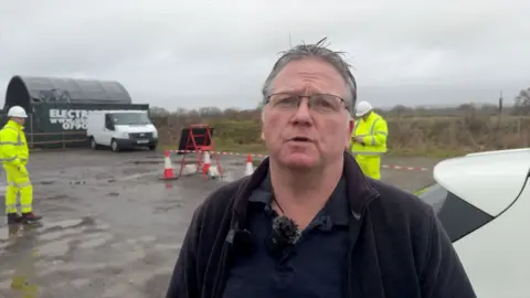 Man with grey hair and black jacket standing outdoors 