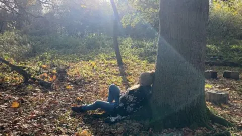 A woman sat with her back against a tree staring into the distance 