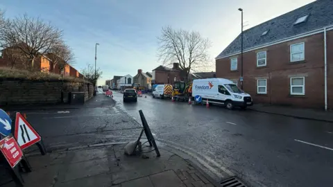 Road with vans on it. It is a clear blue sky. Roadwork signs are on the road. 