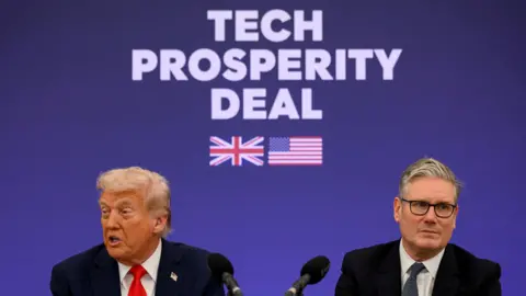 Reuters US President Donald Trump and British Prime Minister Keir Starmer seated in front of microphones at a press conference. "Tech Prosperity Deal" is emblazoned in large, white text on a blue backdrop behind them with pictures of UK and USA flags.