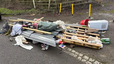 Martin Heath/BBC A pile of rubbish at the side of a road, encroaching on the carriageway, including packets of food, lengths of wood, a pallet, some blankets, a red bucket and an air conditioning unit.
