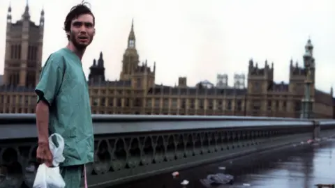 Alamy Cillian Murphy in the 28 Days Later film wearing a pair of scrubs while wandering a deserted London against the backdrop of Parliament in London.