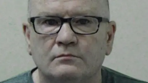 Mugshot of Campbell. He is bald and clean shaven and is wearing black-framed glasses.