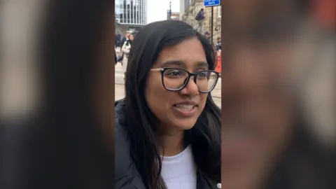 A woman with long dark hair wearing glasses.