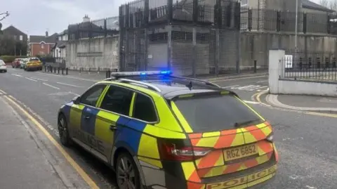 A yellow and blue police car parked outside Strabane police station