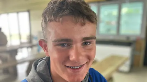 Sir James Smith's School pupil Tallan smiling with braces on his teeth. He is wearing a blue and grey hoodie.