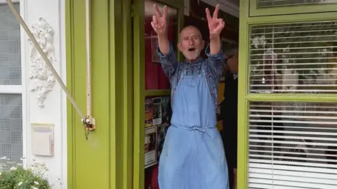 BBC Joe Public gives the peace sign outside his shop