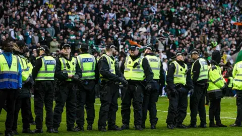 SNS A line of police officers on the pitch at Ibrox. The stands are filled with fans.