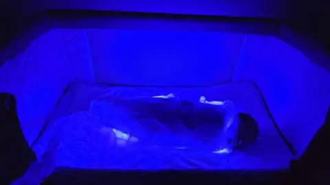 PA Media Baby in the sleeping bag in a cot. The whole thing is lit up in blue 